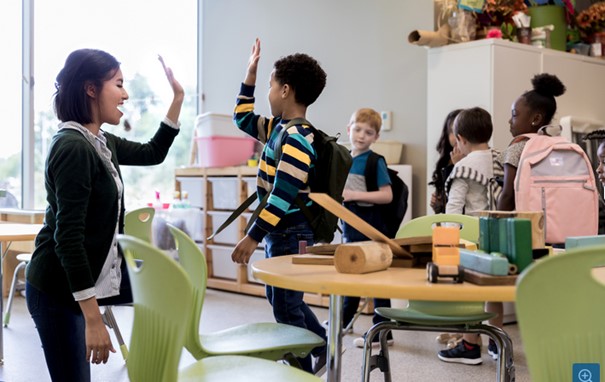 Junge Erzieherin gibt einem Jungen ein High-5, die Klasse steht dahinter.